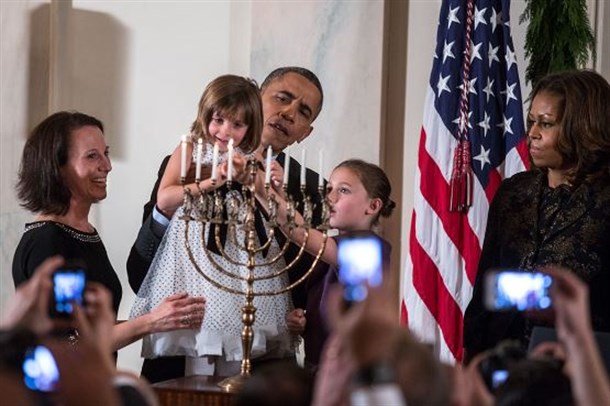 President Barack Obama holds up Kylie Schmitter as she and her sister Lainey Schmitter light the menorah during the Hanukkah reception in the Grand Foyer of the White House, Dec. 5, 2013. (Official White House Photo by Lawrence Jackson)